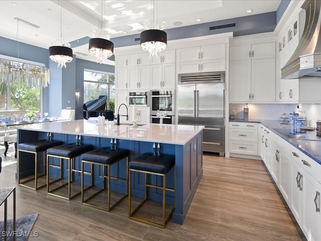 kitchen featuring an inviting chandelier, a spacious island, hanging light fixtures, wall chimney exhaust hood, and stainless steel appliances