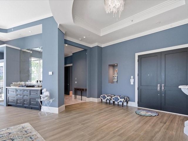 entryway with light wood-type flooring, a tray ceiling, and ornamental molding