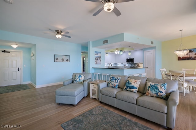 living room with hardwood / wood-style floors, ceiling fan with notable chandelier, and sink