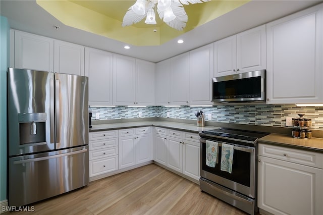 kitchen with appliances with stainless steel finishes, tasteful backsplash, ceiling fan, light hardwood / wood-style flooring, and white cabinets