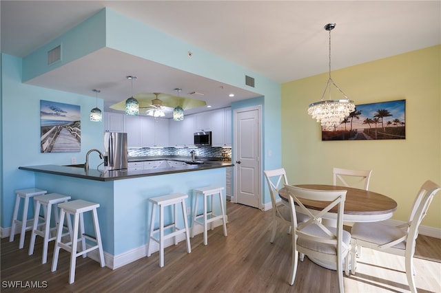 kitchen featuring hardwood / wood-style floors, pendant lighting, a kitchen bar, decorative backsplash, and appliances with stainless steel finishes