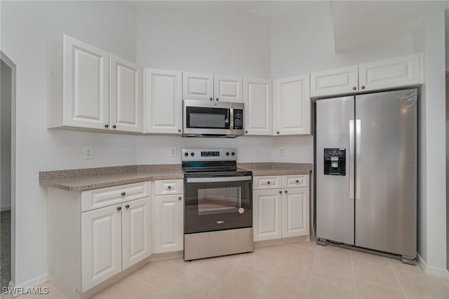 kitchen featuring light tile patterned floors, white cabinetry, appliances with stainless steel finishes, and a towering ceiling