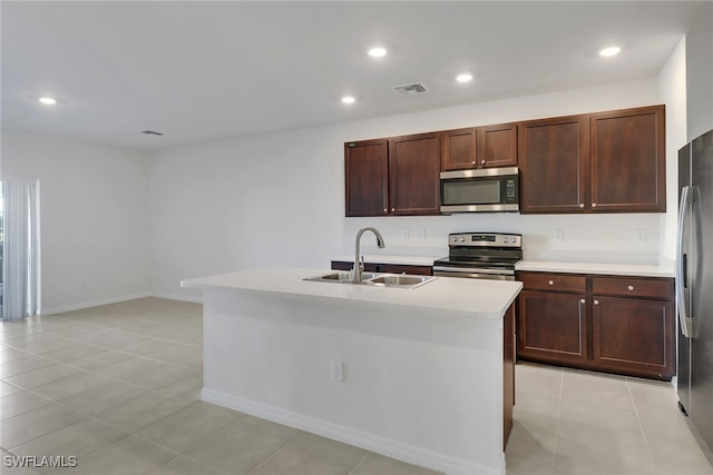 kitchen with appliances with stainless steel finishes, light tile patterned floors, a kitchen island with sink, and sink