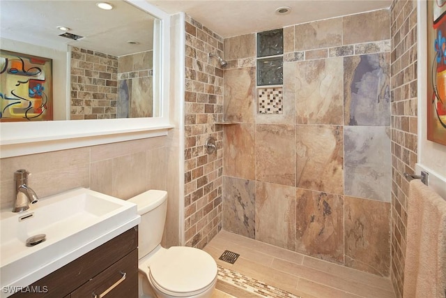 bathroom featuring a tile shower, vanity, toilet, and tile walls