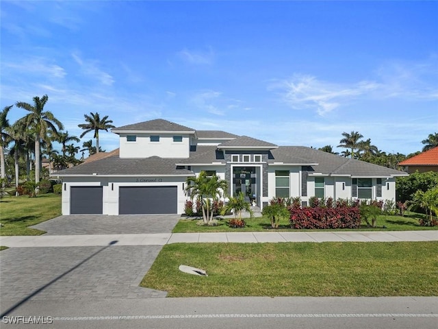 prairie-style home with a garage, decorative driveway, a front yard, and stucco siding