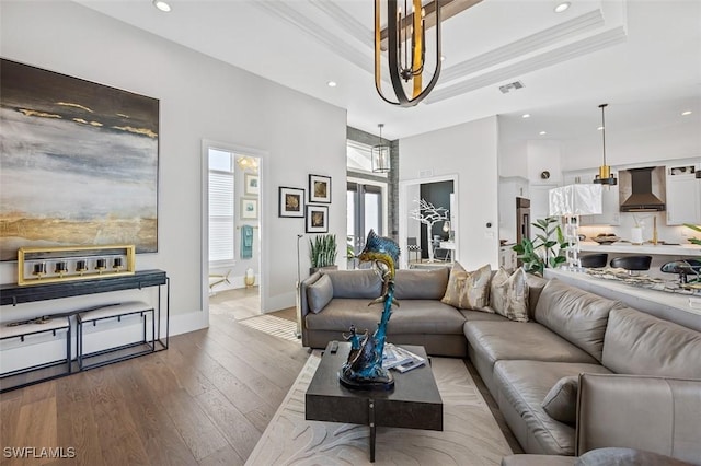 living room with wood finished floors, a raised ceiling, visible vents, and crown molding