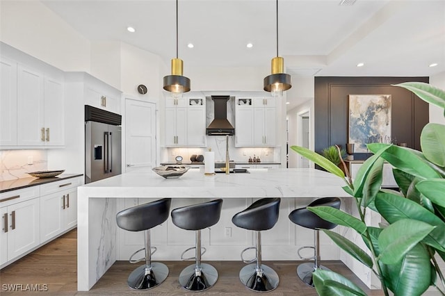 kitchen featuring high end fridge, decorative light fixtures, wall chimney range hood, and light stone countertops