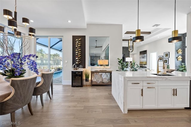 kitchen featuring ceiling fan, hanging light fixtures, beverage cooler, white cabinets, and light wood-type flooring