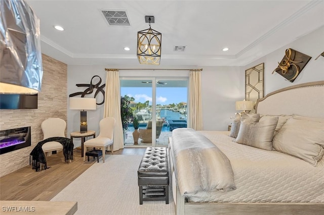 bedroom featuring hardwood / wood-style floors, a water view, access to exterior, ornamental molding, and a fireplace