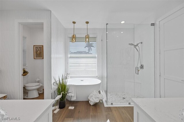 bathroom featuring a soaking tub, toilet, a stall shower, vanity, and wood finished floors