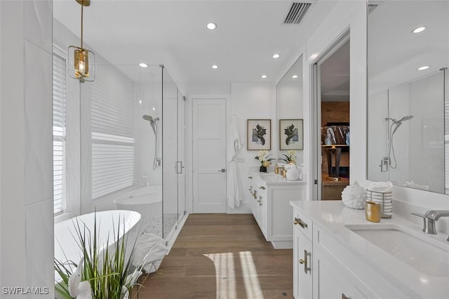 full bathroom featuring visible vents, wood finished floors, a sink, a shower stall, and two vanities