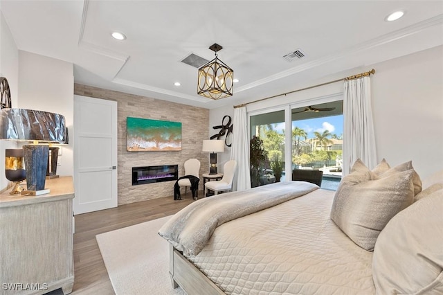 bedroom featuring a large fireplace, hardwood / wood-style floors, a tray ceiling, a chandelier, and access to outside