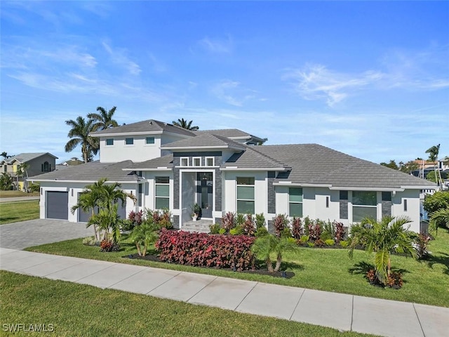 prairie-style house featuring an attached garage, decorative driveway, a front yard, and stucco siding