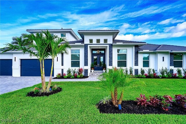 prairie-style home with french doors, stucco siding, decorative driveway, and a front lawn