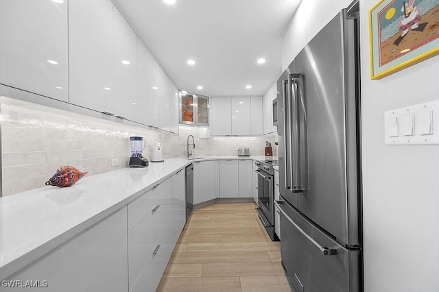 kitchen featuring decorative backsplash, light wood-type flooring, stainless steel appliances, sink, and white cabinetry