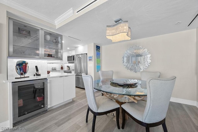 dining space with indoor bar, light hardwood / wood-style floors, beverage cooler, and ornamental molding