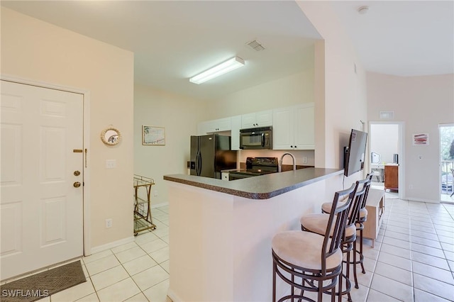 kitchen featuring black appliances, a kitchen breakfast bar, kitchen peninsula, light tile patterned floors, and white cabinetry