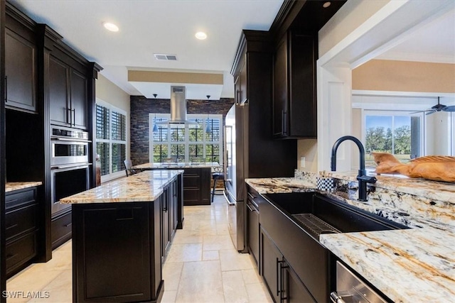 kitchen with light stone countertops, island exhaust hood, double oven, sink, and a kitchen island