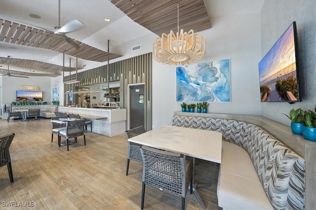 dining room with a towering ceiling, wood ceiling, ceiling fan with notable chandelier, and light wood-type flooring