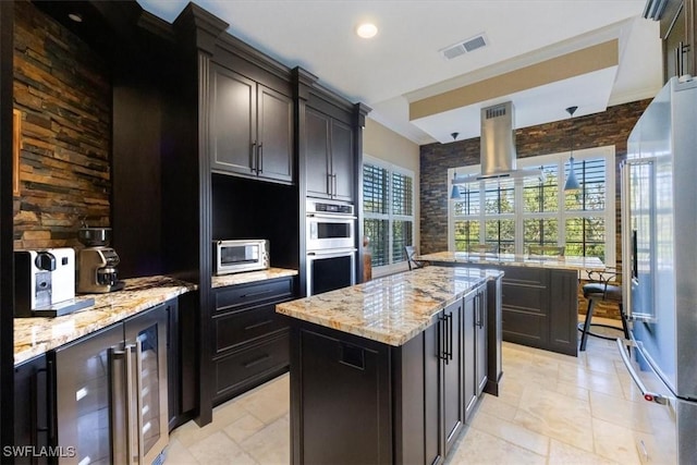 kitchen featuring light stone countertops, high quality fridge, stainless steel double oven, and a kitchen island