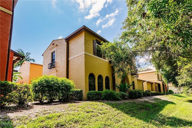 view of side of home with a lawn, a balcony, and stucco siding