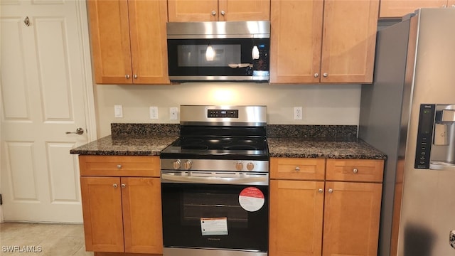 kitchen featuring light tile patterned floors, appliances with stainless steel finishes, and dark stone counters