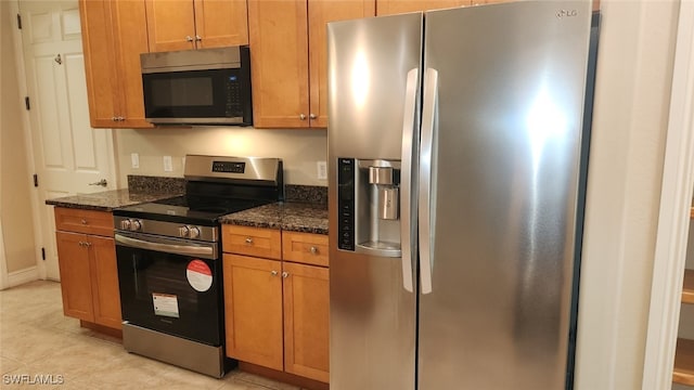 kitchen featuring appliances with stainless steel finishes, dark stone counters, and light tile patterned flooring