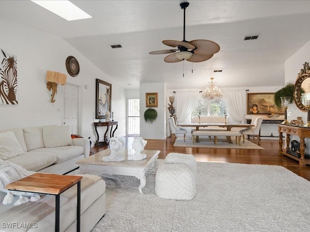 living room with ceiling fan with notable chandelier, wood-type flooring, and lofted ceiling with skylight