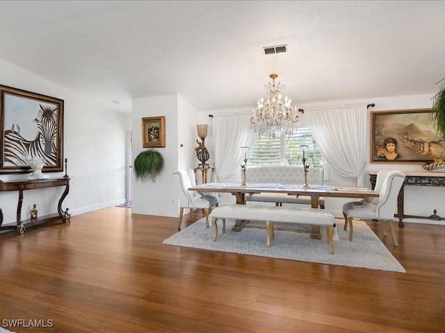 dining area with dark wood-type flooring and an inviting chandelier