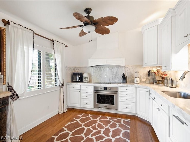 kitchen featuring sink, premium range hood, backsplash, oven, and white cabinets