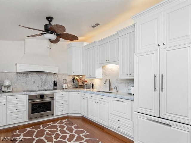 kitchen with stainless steel oven, custom range hood, sink, and white cabinetry