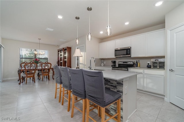 kitchen featuring a kitchen island with sink, a kitchen breakfast bar, hanging light fixtures, appliances with stainless steel finishes, and white cabinetry