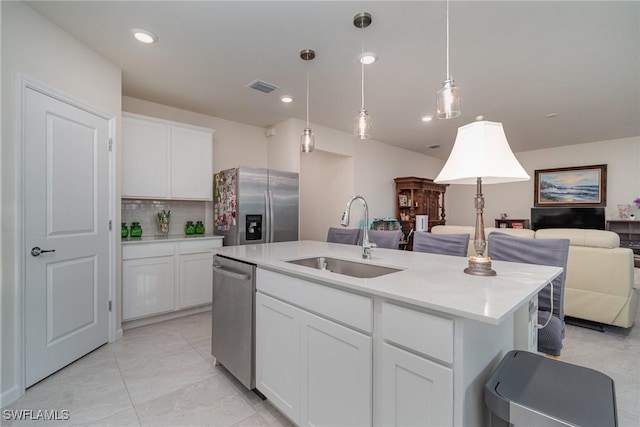 kitchen with a center island with sink, white cabinets, sink, appliances with stainless steel finishes, and decorative light fixtures