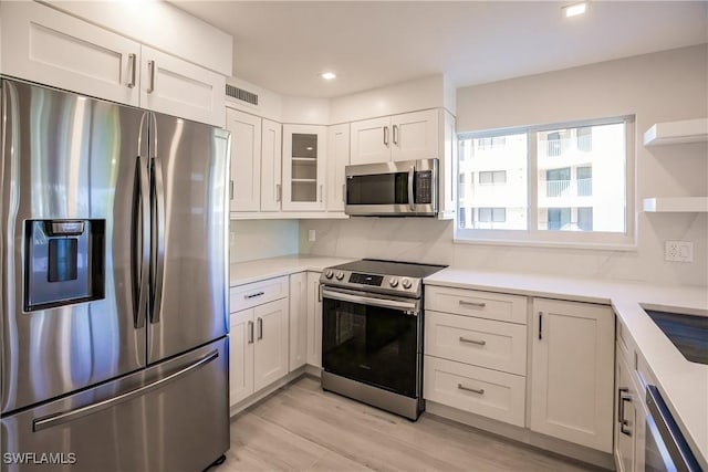 kitchen featuring decorative backsplash, light hardwood / wood-style flooring, white cabinets, and appliances with stainless steel finishes