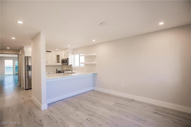 kitchen featuring kitchen peninsula, stainless steel appliances, sink, light hardwood / wood-style flooring, and white cabinets