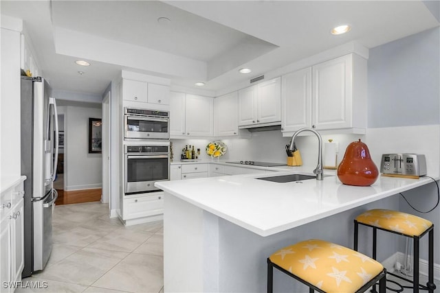 kitchen with kitchen peninsula, a kitchen bar, stainless steel appliances, sink, and white cabinets