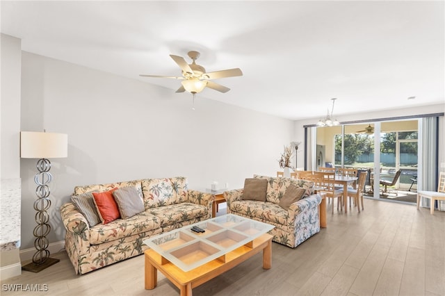 living room featuring ceiling fan with notable chandelier and light wood-type flooring