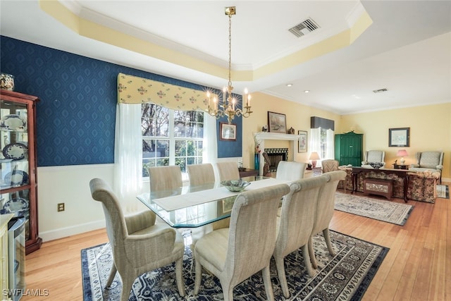 dining room featuring a raised ceiling, light wood-type flooring, ornamental molding, and a chandelier