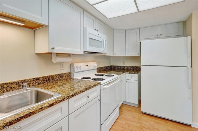 kitchen with white cabinetry, sink, dark stone countertops, light hardwood / wood-style floors, and white appliances