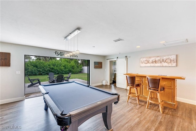 game room featuring a barn door, light hardwood / wood-style floors, pool table, and bar area