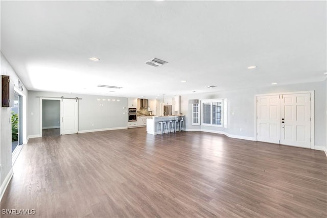unfurnished living room featuring visible vents, baseboards, recessed lighting, and a barn door
