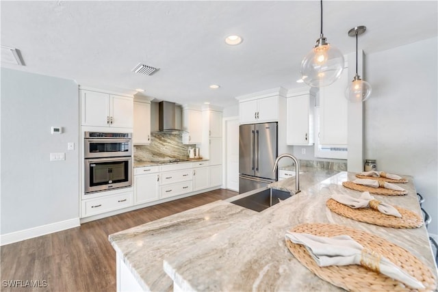 kitchen with a peninsula, appliances with stainless steel finishes, wall chimney exhaust hood, and white cabinets