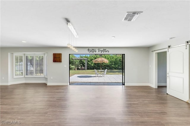 unfurnished living room with wood finished floors, baseboards, visible vents, and a barn door