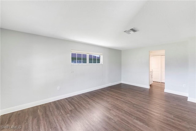 spare room with dark wood-type flooring, visible vents, and baseboards