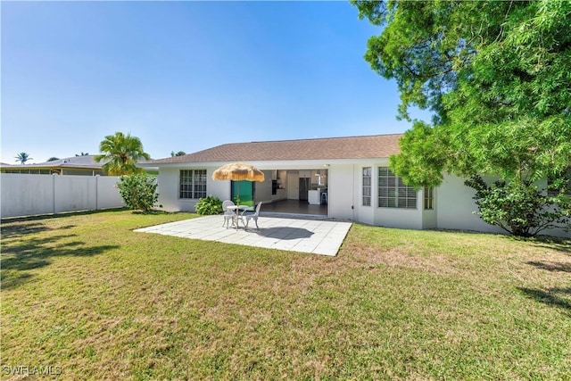 rear view of house featuring a patio area, stucco siding, fence, and a lawn