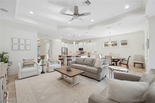 living room featuring a tray ceiling, crown molding, light tile patterned floors, and ceiling fan with notable chandelier