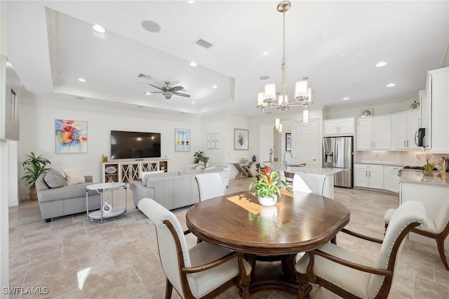 dining area featuring ceiling fan with notable chandelier, a raised ceiling, and sink