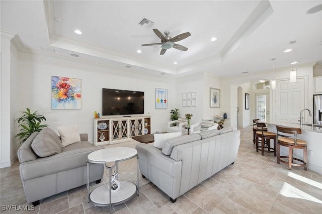 living room featuring a tray ceiling, ceiling fan, and ornamental molding