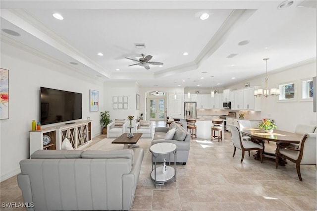 living room with a raised ceiling, crown molding, plenty of natural light, and ceiling fan with notable chandelier