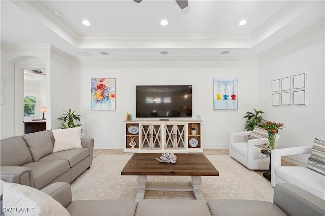 living room with a raised ceiling, ceiling fan, and ornamental molding